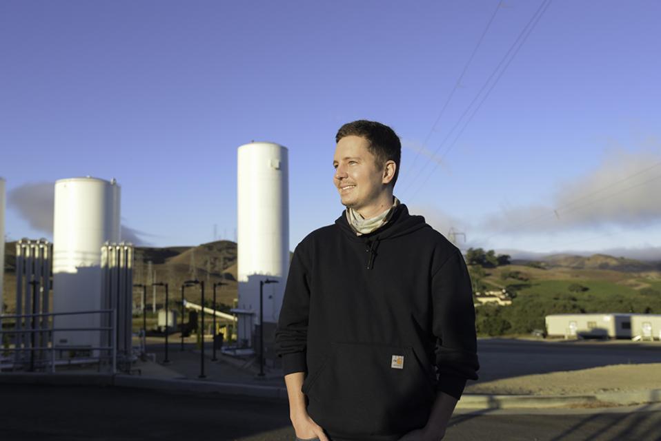 A smiling Zone 7 employee looking off to the left with the sun shining on him. Water treatment plant in the background