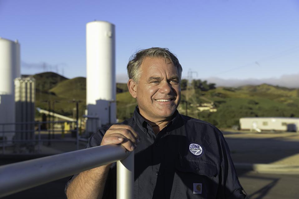 Zone 7 Employee smiling while the sun is shining on him, Water tower at Del Valle Water Treatment is in the background
