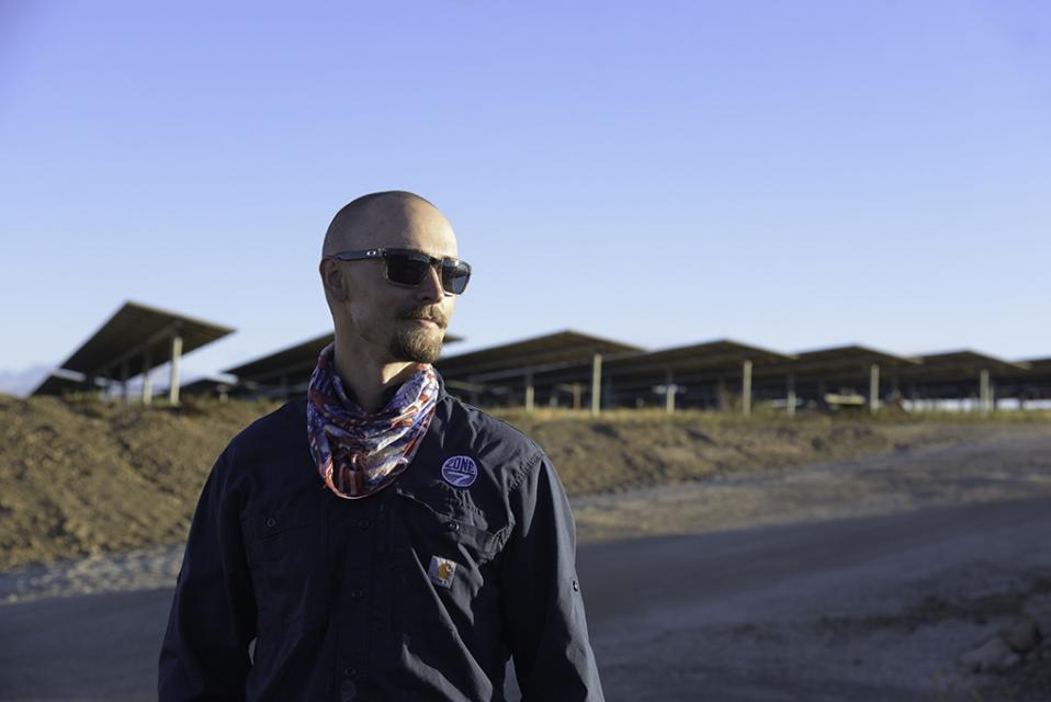 A Zone 7 employee wearing sunglasses and looking off to the right, and a solar power installation in the background