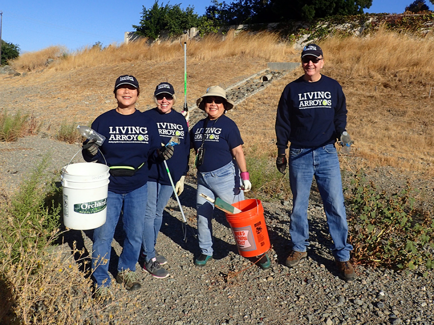 Four smiling Living Arroyos volunteers participating in a creek cleanup event