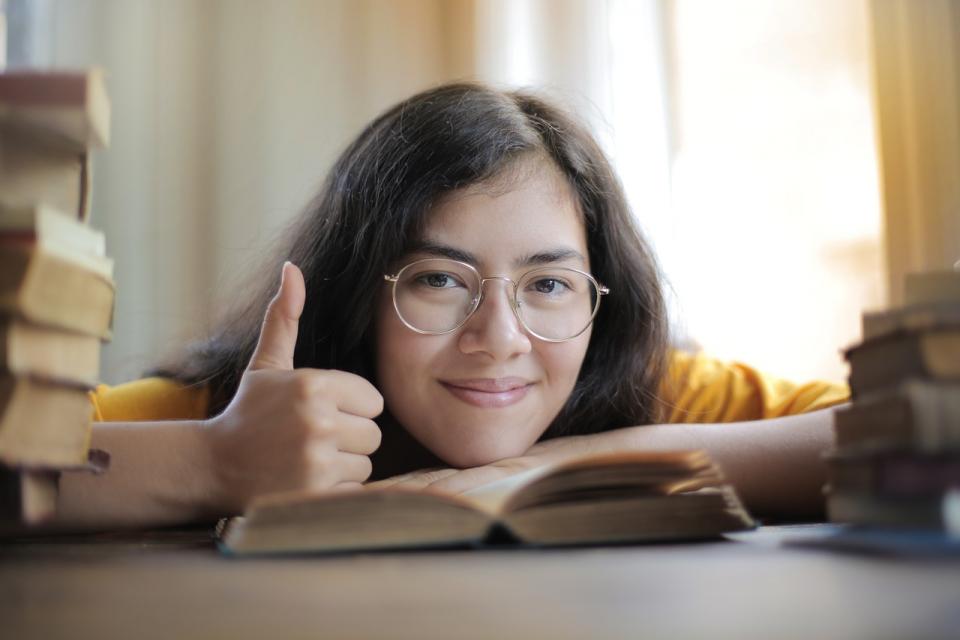 Student giving a thumbs up next to a pile of books