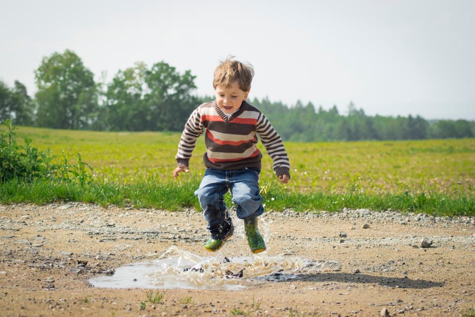 A child  wearing rain boots jumping into a puddle