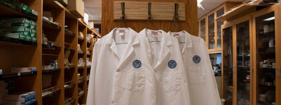 Three Zone 7 white lab coats hanging on a wall.