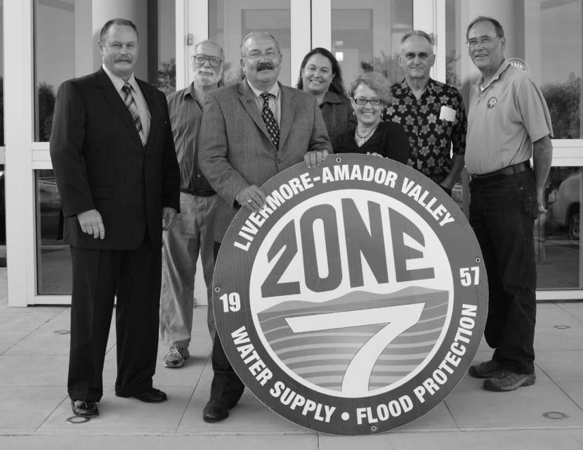 Black and white photo of seven of Zone 7 Water Agency's Board of Directors standing behind large circular logo of Zone 7