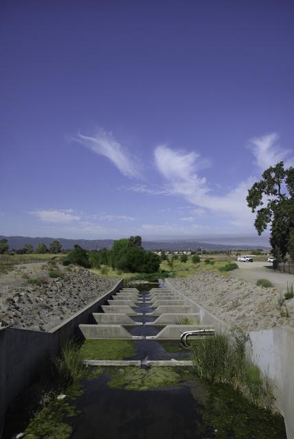 A fish ladder with shrubs and a mountain ridge in the background.