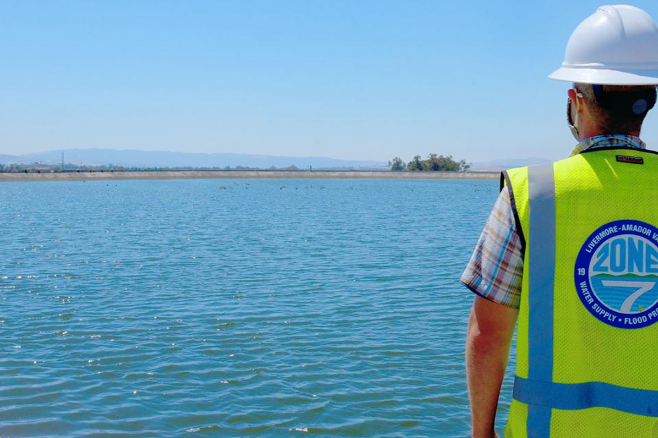 Zone 7 Engineer wearing a white hard hat and a yellow hazard vest looking out to a body of water
